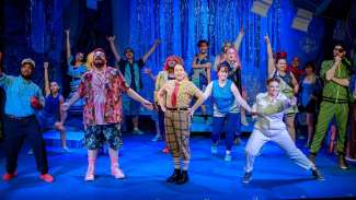 Performers stand on a stage with their arms outreached